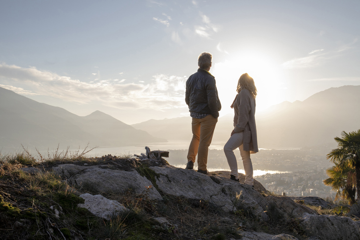 Two older adults gazing across a small village vista as the sun sets.